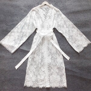 May include: White lace robe with long sleeves and a tie belt. The robe is sheer and has a delicate floral pattern.