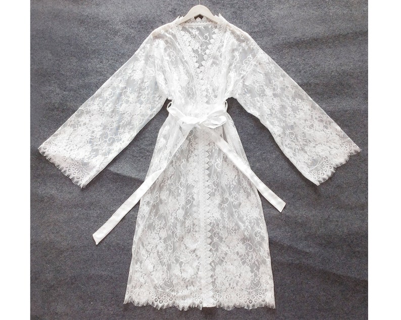 May include: White lace robe with long sleeves and a tie belt. The robe is sheer and has a delicate floral pattern.