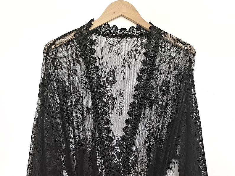 May include: Black lace robe with a V-neckline and long sleeves. The robe is made of delicate, sheer lace and has a floral pattern.