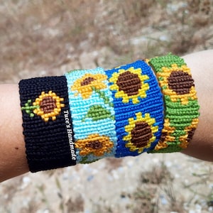 May include: Four friendship bracelets with sunflower designs. The bracelets are made with colorful embroidery floss and feature black, blue, green, and light blue colors. The text "Tuce's Handmade" is visible on the black bracelet.