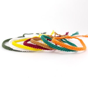 May include: A set of seven colorful braided bracelets in green, white, yellow, red, brown, teal, and orange.