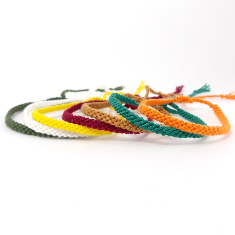 May include: A set of seven colorful braided bracelets in green, white, yellow, red, brown, teal, and orange.