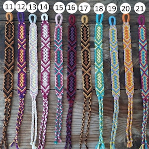 May include: A set of 11 colorful friendship bracelets with different geometric patterns. The bracelets are made with colorful embroidery floss and have a knotted fringe at the ends. The bracelets are numbered 11 through 21.