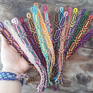 May include: A collection of colorful friendship bracelets with geometric patterns. The bracelets are made with colorful embroidery floss and have tassels at the ends.