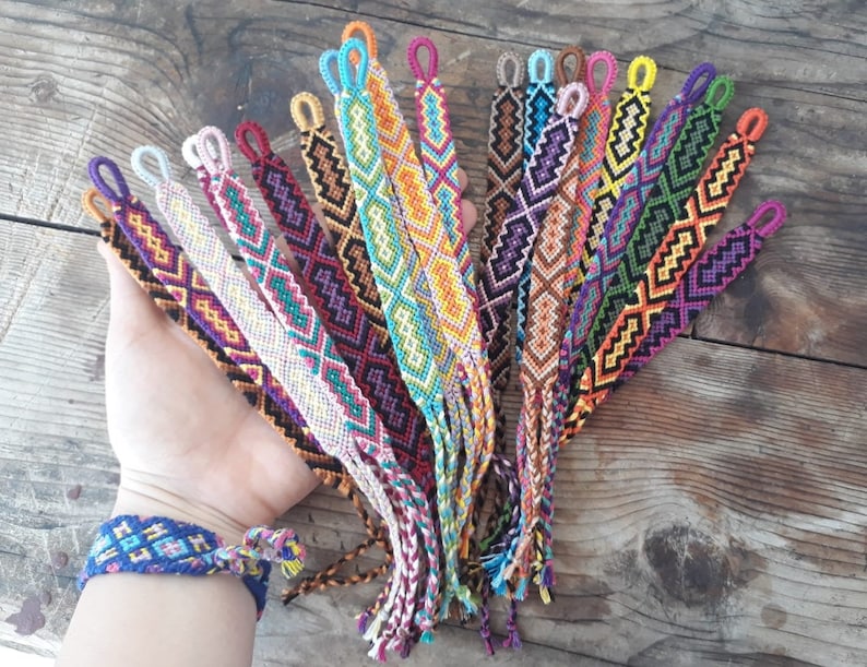 May include: A collection of colorful friendship bracelets with geometric patterns. The bracelets are made with colorful embroidery floss and have tassels at the ends.