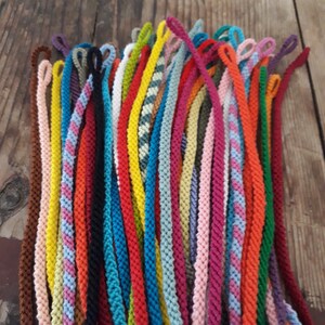 May include: A collection of colorful braided cords with loops at the end. The cords are arranged in a fan shape and are made of various colors, including red, blue, green, yellow, and pink.