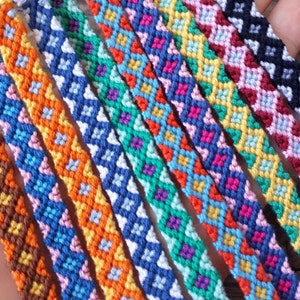 Könnte beinhalten: Eine Sammlung bunter Freundschaftsbänder mit geometrischen Mustern. Die Armbänder sind aus verschiedenen farbigen Fäden gefertigt und weisen eine Vielzahl von rautenförmigen Designs auf.