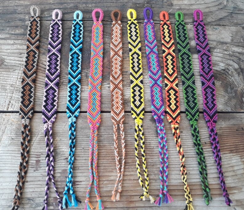 May include: A set of ten colorful friendship bracelets with various geometric patterns. The bracelets are made with colorful embroidery floss and have a knotted fringe at the ends.