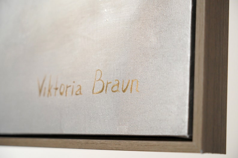 May include: Close-up of a white canvas with a gold signature that reads "Viktoria Braun". The canvas is framed in a light brown wood frame.