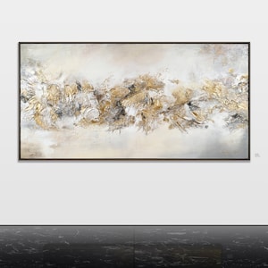May include: Abstract painting with a white background and gold and gray accents. The painting is framed in a black frame.