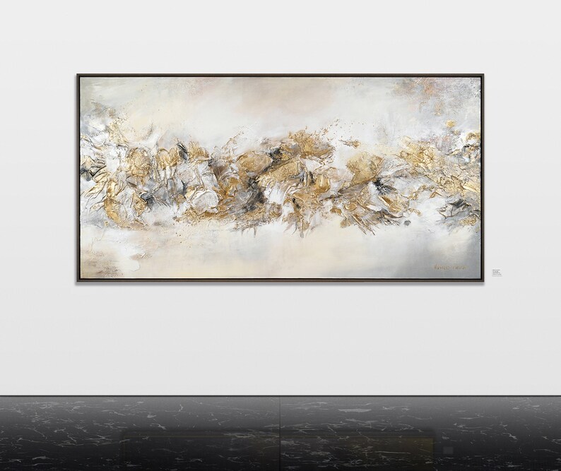 May include: Abstract painting with a white background and gold and gray accents. The painting is framed in a black frame.