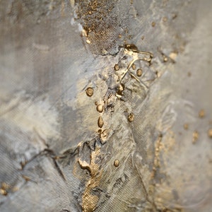 May include: Abstract painting with a textured, gray background and gold accents. The gold paint is applied in a dripping and splattered pattern, creating a dynamic and modern look.
