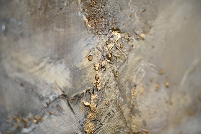 May include: Abstract painting with a textured, gray background and gold accents. The gold paint is applied in a dripping and splattered pattern, creating a dynamic and modern look.