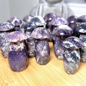 May include: A group of amethyst mushroom ornaments. The mushroom caps are a lighter shade of purple, while the stems are a darker shade. The ornaments are displayed on a wooden surface.