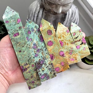 May include: Five green and pink ruby in zoisite crystal points, also known as ruby zoisite, arranged in a row. The points are polished and have a smooth, shiny surface.