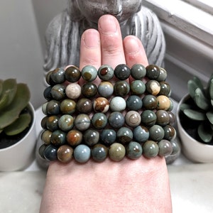May include: A stack of eight bracelets made with green, brown, and beige jasper beads.