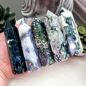 May include: Five polished crystal towers arranged in a row. The stones feature varied patterns of deep forest green, translucent white, and mossy inclusions. Each tower has a hexagonal base and a pointed top, displaying natural mineral textures.