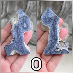 May include: A polished, irregular mineral specimen featuring a deep blue, porous, and fibrous crystalline structure contrasted with sections of light beige, textured stone. The piece displays a pointed top and a jagged, organic silhouette.