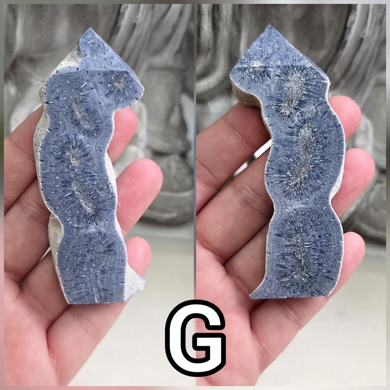 May include: A polished, elongated mineral specimen featuring a deep blue, textured surface with distinct, radiating star-like patterns throughout. The stone has a curved, irregular shape with a pointed top and a rough, light-colored outer edge.