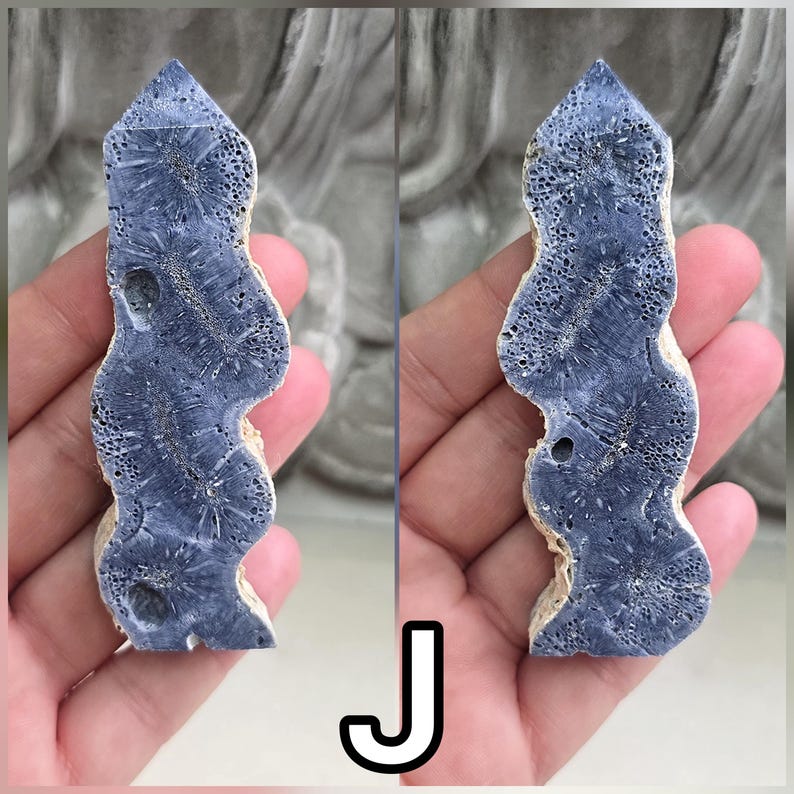 May include: A tall, slender, pointed crystal tower with a wavy, organic silhouette. The surface features a deep blue, porous, and textured pattern with radiating star-like formations and small natural indentations throughout the stone structure.