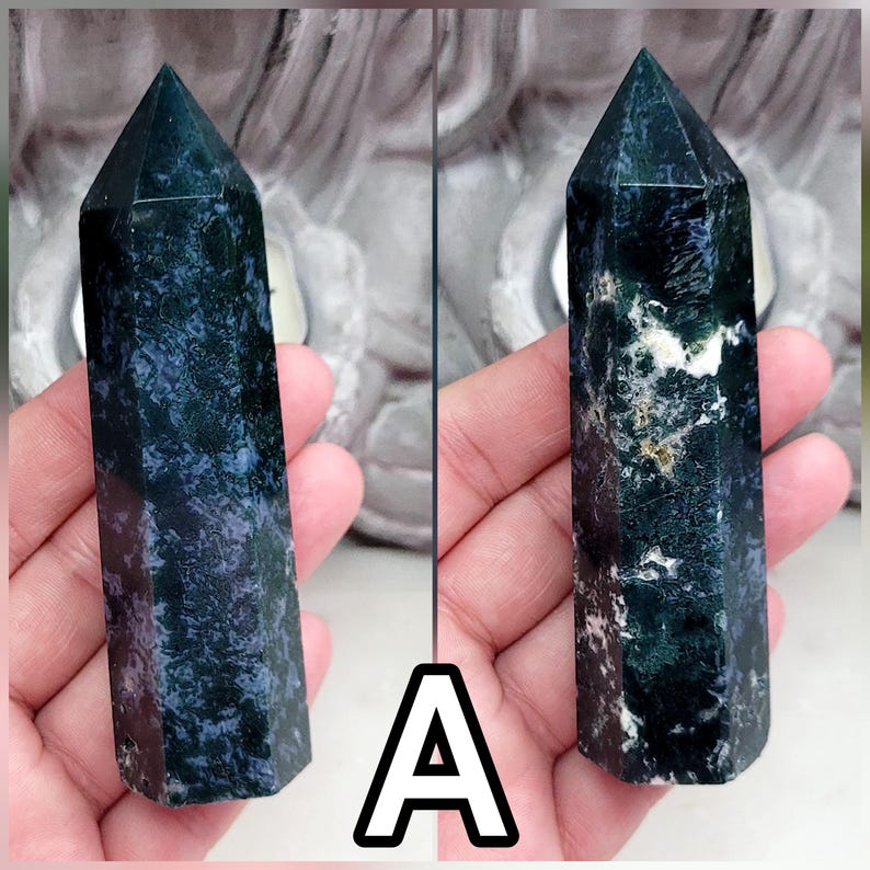 May include: A polished, hexagonal crystal tower featuring a deep forest green and dark blue mottled surface with scattered white inclusions. The stone has a pointed top and a smooth, reflective texture, displaying natural mineral patterns throughout.
