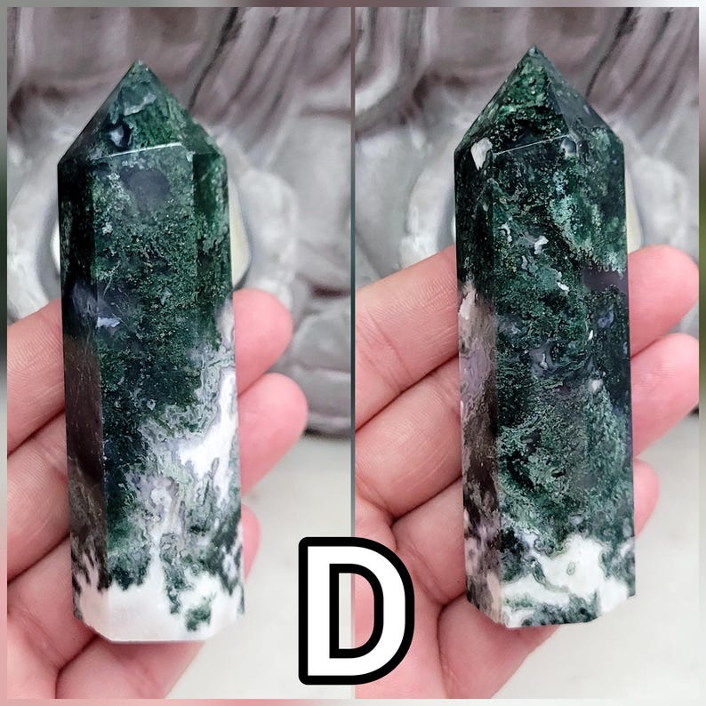 May include: A polished moss agate crystal tower featuring a hexagonal prism shape with a pointed top. The stone displays deep forest green moss-like inclusions, translucent areas, and opaque white mineral patterns throughout the entire structure.