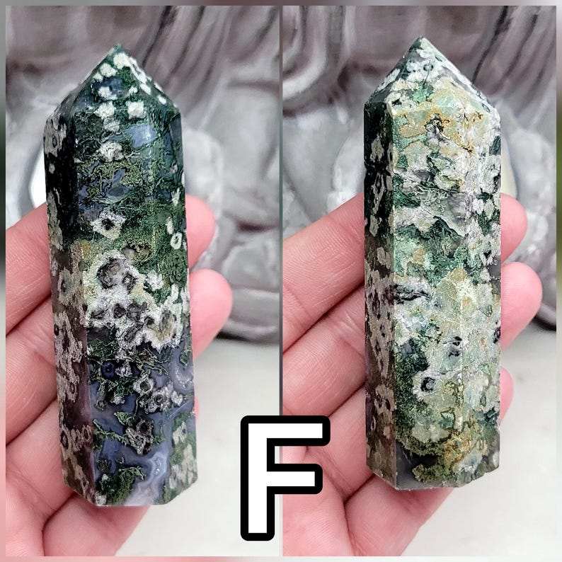 May include: A polished moss agate crystal tower featuring a hexagonal point. The stone displays a complex pattern of deep forest green, translucent gray, and creamy white inclusions, with moss-like dendritic formations throughout the mineral structure.