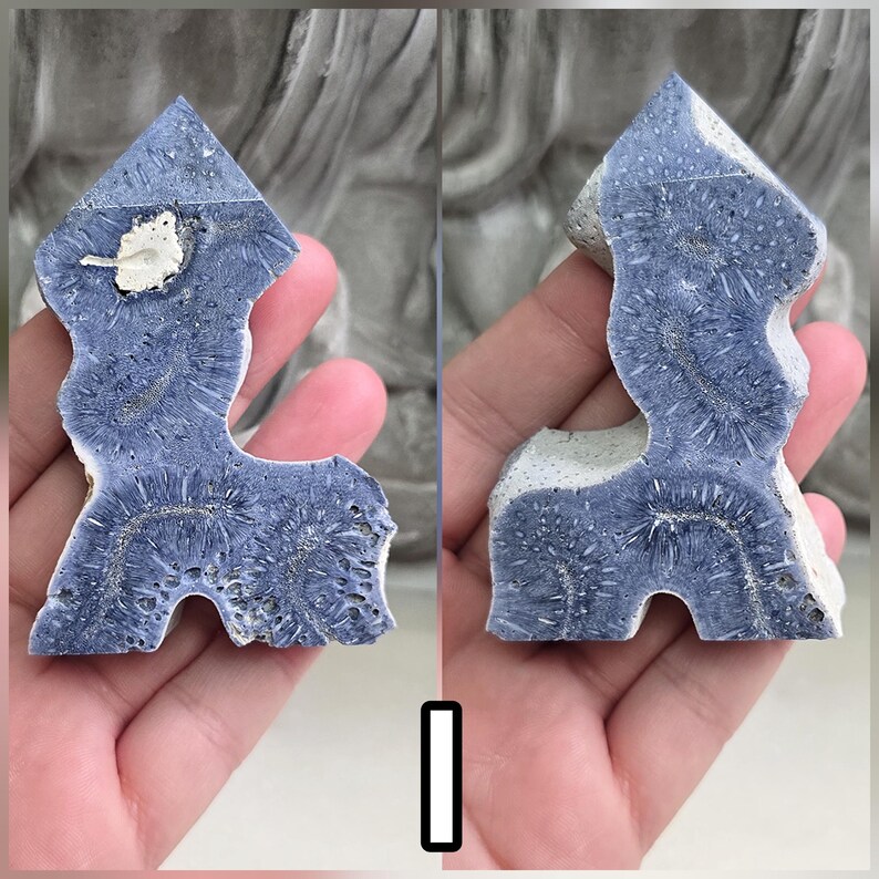 May include: A polished slab of blue lace agate with a jagged, irregular shape. The stone features deep blue, fibrous, fan-like patterns radiating from central lines, with patches of white, porous mineral inclusions along the edges and surface.
