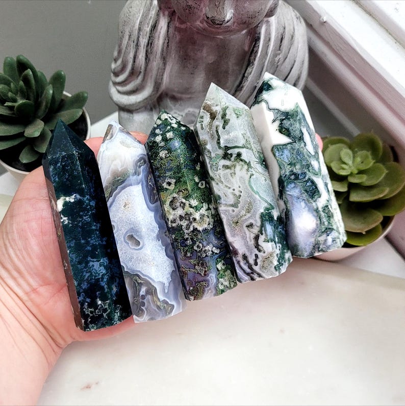 May include: Five polished crystal towers arranged in a row. The stones feature varied patterns of deep forest green, translucent white, and mossy inclusions. Each tower has a hexagonal base and a pointed top, displaying natural mineral textures.