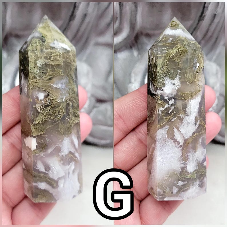 May include: A polished moss agate crystal tower featuring a hexagonal point and a smooth, multifaceted surface. The stone displays a translucent, cloudy white base with intricate, moss-like inclusions in shades of olive green and earthy brown.