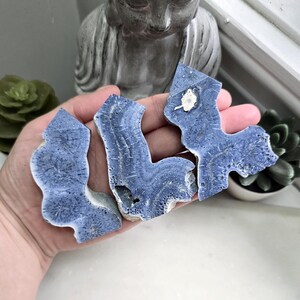 May include: Three flat, irregular slices of blue mineral stone with a radiating, star-like crystalline pattern. The stones feature deep blue hues, textured surfaces, and jagged edges, with one piece displaying a small, distinct white inclusion.