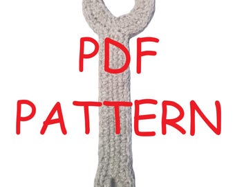 May include: A crocheted wrench in light gray, with the words "PDF PATTERN" in red. The wrench is designed with a loop at the bottom and a curved opening at the top, resembling a real tool. The background is plain white.
