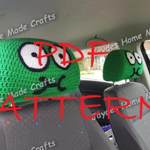 May include: Two green crocheted car headrests with a cartoon face design. The headrests have white eyes, black eyebrows, and a black mouth. The text "PDF PATTERN" is written in red across the image.