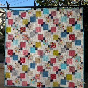 May include: A patchwork quilt with a white background and squares of various colors, including red, pink, blue, green, and yellow. The squares are arranged in a diagonal pattern.
