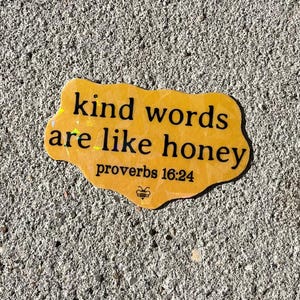May include: A yellow sticker with the quote "kind words are like honey" and the Bible verse Proverbs 16:24. The sticker has a unique shape and a small bee illustration at the bottom.
