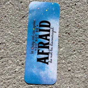 May include: A rectangular bookmark with a blue and white galaxy-inspired background featuring holographic star accents. The text reads: be strong and courageous, DO NOT BE AFRAID, do not be discouraged. The bookmark has rounded corners and a smooth finish.