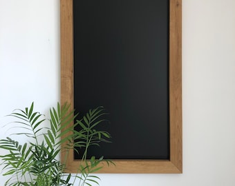 May include: A black chalkboard with a wooden frame, hanging on a white wall. A green plant is in the foreground.
