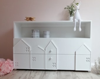 Une commode blanche unique et solide pour un enfant avec des tiroirs en forme de maisons. Une commode pour enfants unique et sûre avec