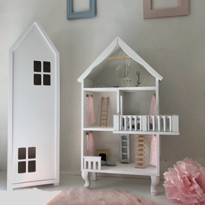 May include: White wooden dollhouse with a pink rug, a pink flower, and two white frames on the wall. The dollhouse has a balcony, a ladder, and a fireplace.