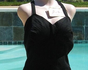 May include: A black swimsuit with a halter top and a fitted skirt. The swimsuit has a simple design and is made of a smooth fabric.