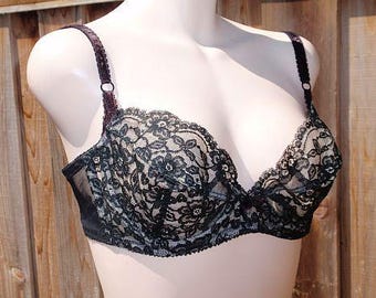 May include: A black lace bra with a floral pattern is displayed on a mannequin. The bra has adjustable straps and a sheer mesh panel on the sides. The bra is a dark color with a delicate lace overlay.
