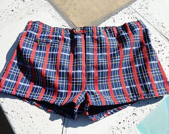 May include: Red and blue plaid swim trunks with a yellow button and a pocket on the side.