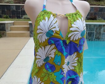 May include: A halter-style swimsuit top with a vibrant floral pattern in white, blue, and purple on a green background. The top is paired with a red bottom. A gold-colored clasp accents the neckline.