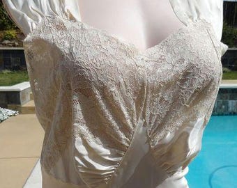 May include: Ivory-colored vintage dress with a lace bodice and satin skirt. The dress features a V-neckline and short, puffed sleeves. The lace detailing adds a delicate texture to the elegant, flowing design.