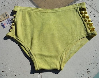 May include: A pair of yellow cotton underwear with a yellow and white braided trim along the sides. The underwear has a high-cut leg.