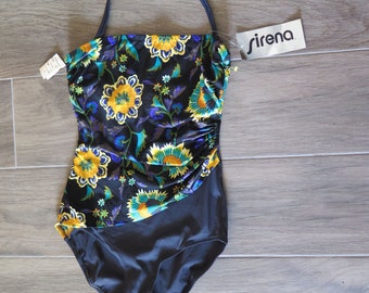 May include: One-piece swimsuit with a floral pattern. The top features a black background with yellow, blue, and green floral designs. The bottom is a solid dark gray. The swimsuit has a halter strap and a tag that says "sirena".