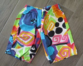 May include: Colorful patterned shorts with a white background and a variety of shapes and colors, including blue, green, yellow, pink, and black.