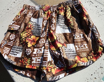 May include: Brown and white patterned shorts with a tropical design. The shorts feature a repeating pattern of pineapples, flowers, and geometric shapes. The elastic waistband is visible at the top.