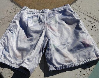 May include: White nylon swim shorts with a subtle pattern. The shorts have an elastic waistband and a drawstring.