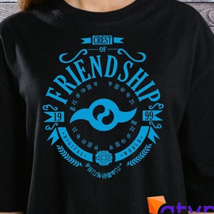 May include: A black t-shirt with a blue and white crest design featuring the words "Crest of Friendship" and the numbers "19" and "99". The crest also includes the words "Digital World" and a stylized symbol.